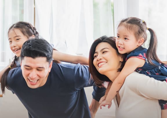 A family of three is sitting on a couch, with the woman in the middle being piggybacked by the two children.