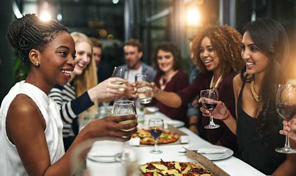 a group of people sitting at a table drinking wine and eating pizza