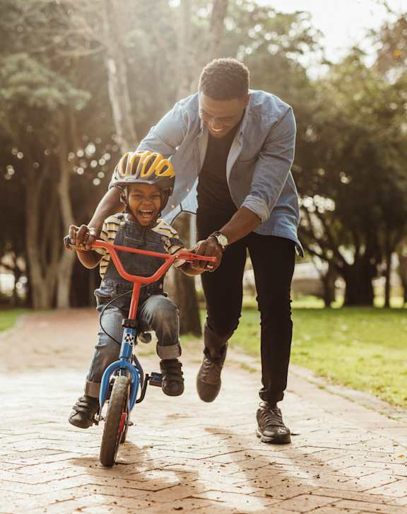 A man is helping a child ride a bike in a park.