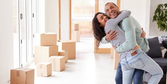 a man and woman hugging in the middle of a room full of cardboard boxes