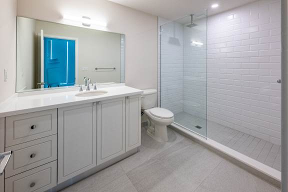 A white bathroom with a blue cabinet and a glass shower door. at The Hamilton Apartments, Miami, FL 33137
