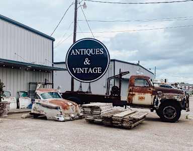 An old rusty truck is parked in front of a building that says Antiques & Vintage.