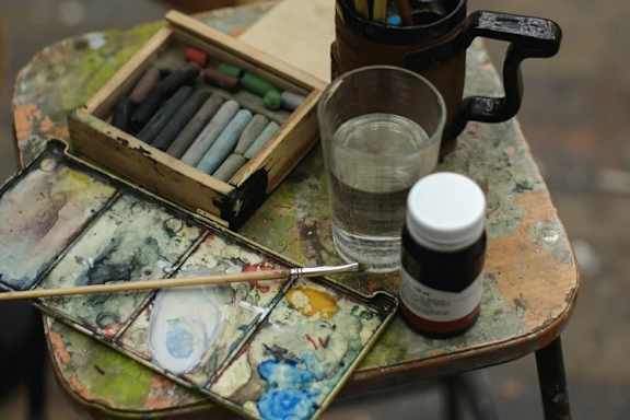 A collection of paint brushes and a cup of water on a table.