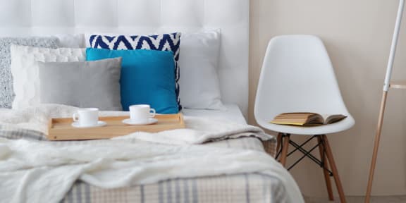 a bed with blue and white pillows and a wooden tray with coffee and a book on