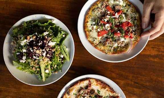 Three dishes, one with a salad, one with pizza, and one with a pizza cut into slices.