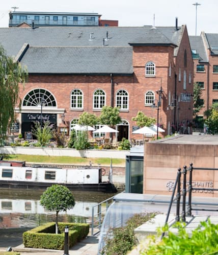 a canal with a boat in front of a large building at The Trilogy Apartments, Manchester, M15 4RU