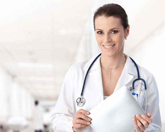 a woman in a white coat holds a piece of paper and smiles at the camera