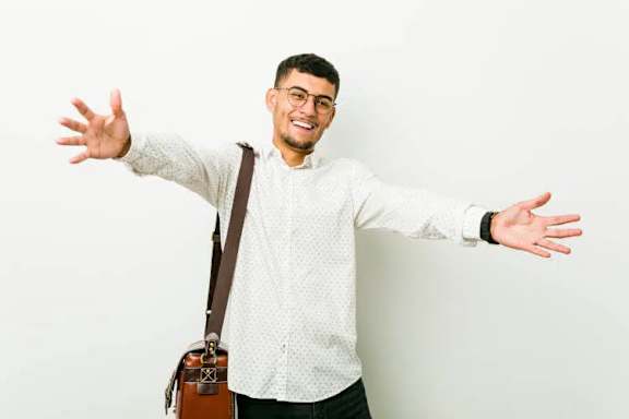 A man with glasses and a white shirt is standing with his arms outstretched.