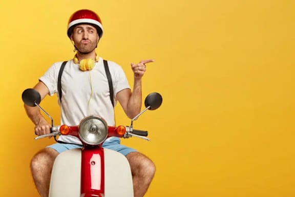 A man in a white shirt and red helmet is sitting on a red and white scooter.