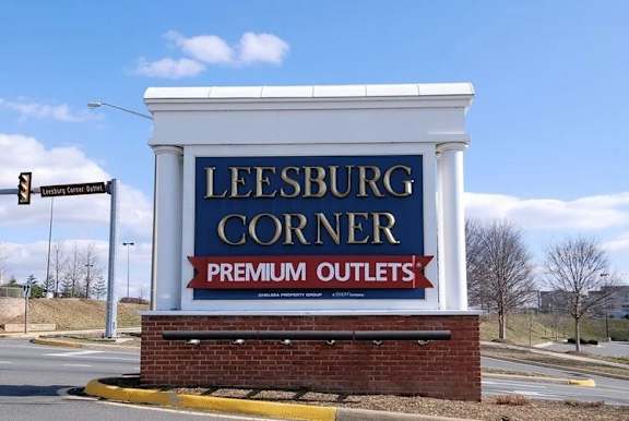 A large sign for Leesburg Corner Premium Outlets stands in front of a traffic light.