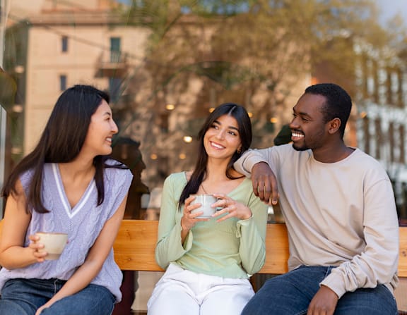 Three people are sitting on a bench, enjoying a conversation and drinks.