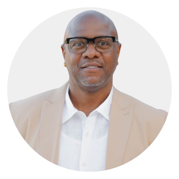 A man with glasses and a beige blazer over a white shirt.