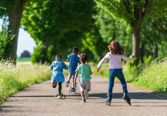 Four children are running down a path with skateboards.