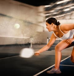 a woman in a white tank top and blue shorts hits a tennis ball with a racquet