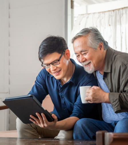 two men sitting on a couch looking at a tablet computer