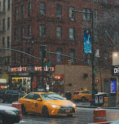 A yellow taxi is driving down a wet street.
