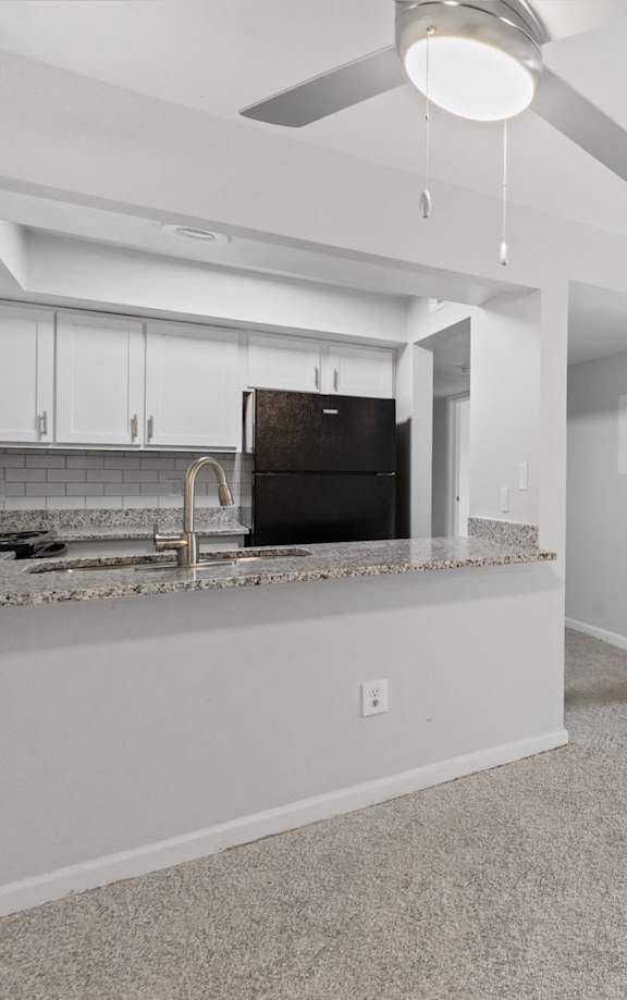 A spacious living room with a ceiling fan and a kitchen area in the background.