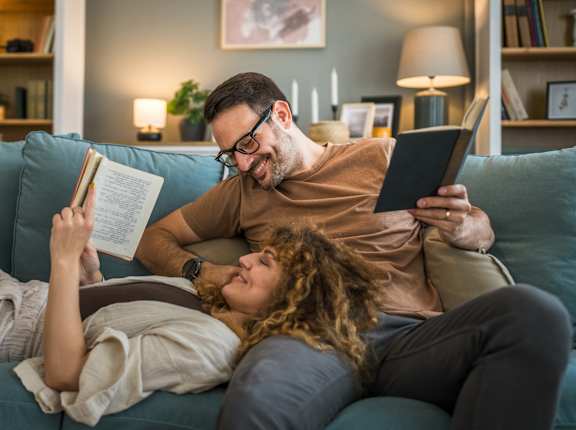 A man and a woman are reading books on a couch.