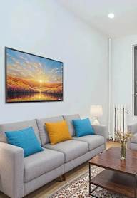 A living room with a grey couch, a painting on the wall, and a window with a view of a building.