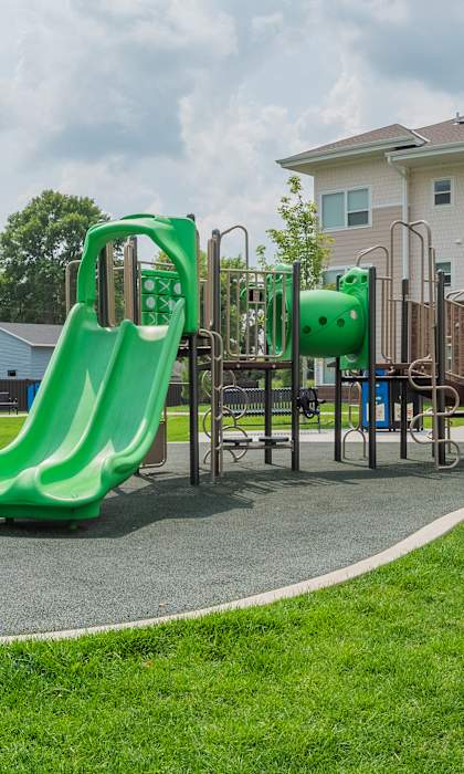 A playground with a green slide in front of a large building.