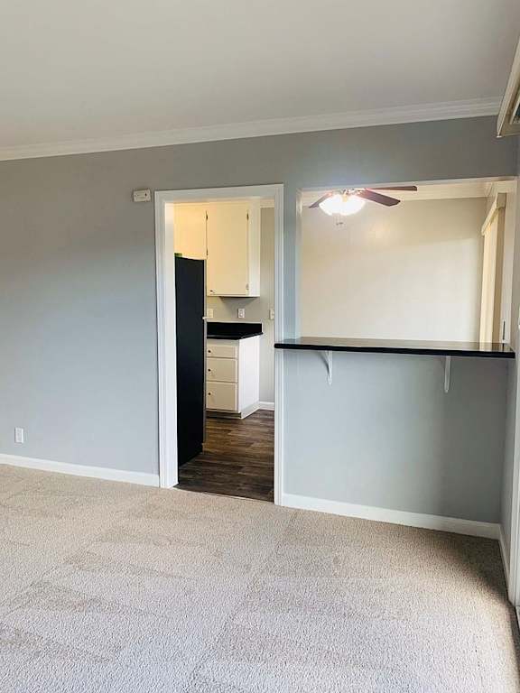 A room with a ceiling fan and a kitchen area in the background.