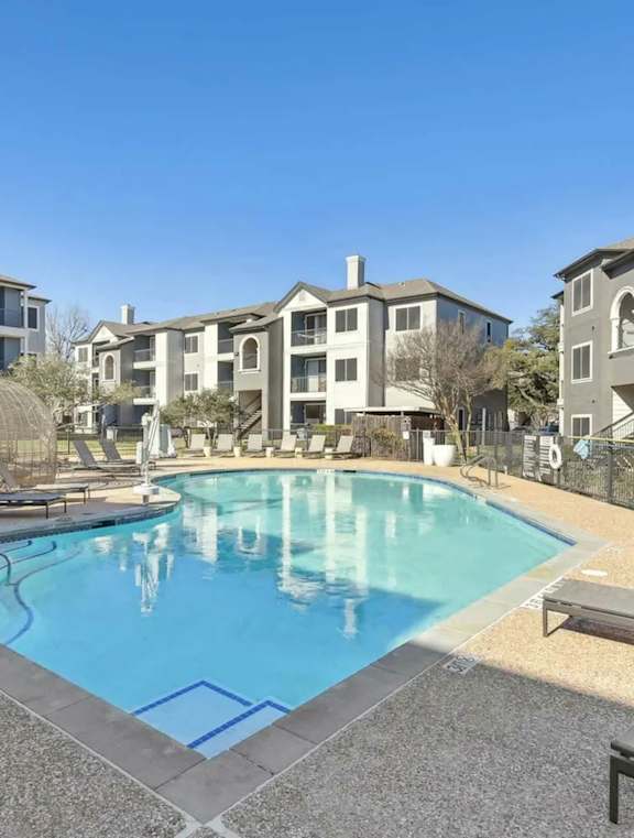 A swimming pool surrounded by a concrete patio and a building in the background.