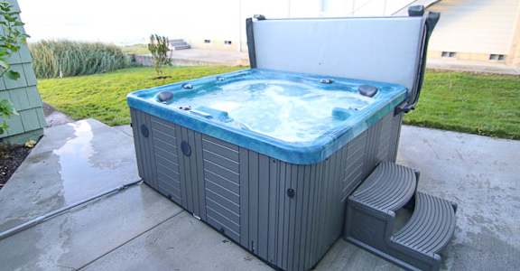 A hot tub with a lid open is placed on a concrete patio.