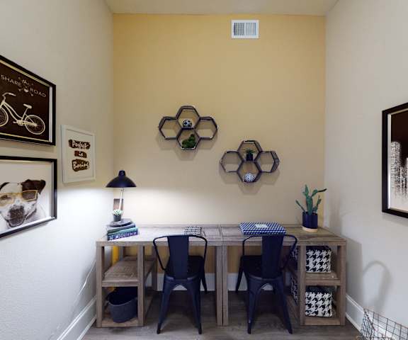 The professional business center with a desk, a computer, comfortable blue chairs, a plant, and wall art at Lofts at Watters Creek Apartments. 