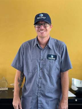A man wearing a blue shirt and a cap with the word "POSTNATURE" on it.