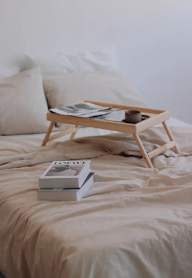 A wooden tray with a book and a cup on a bed.