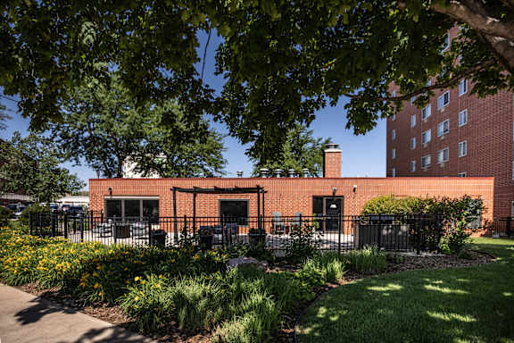 A red brick building with a black fence and green plants in front.