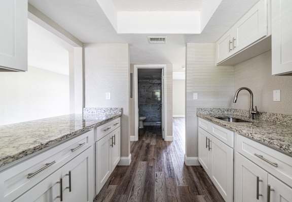 a kitchen with white cabinets and marble counter tops