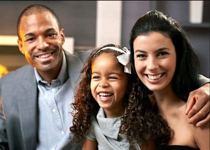 a young girl with a white bow in her hair is sitting with her parents