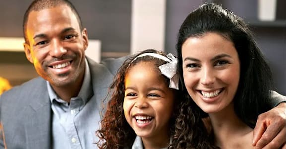 a young girl with a white bow in her hair is sitting with her parents