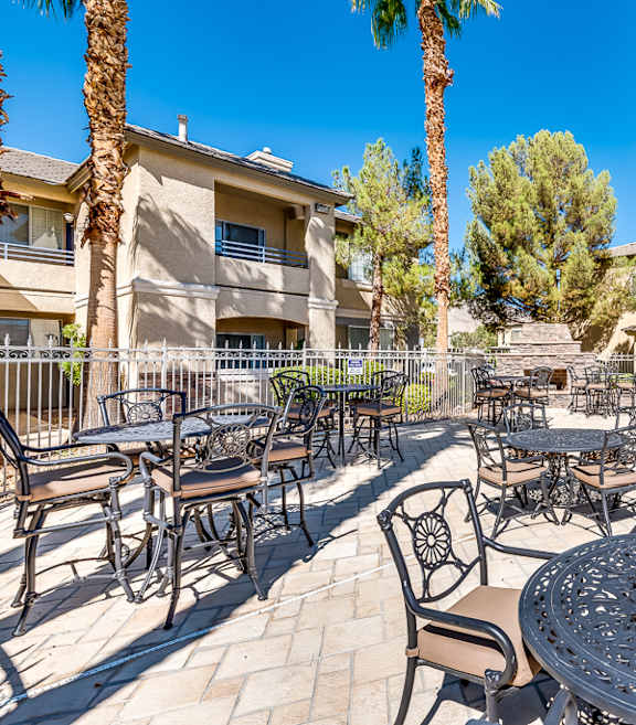 A patio with tables and chairs surrounded by palm trees.