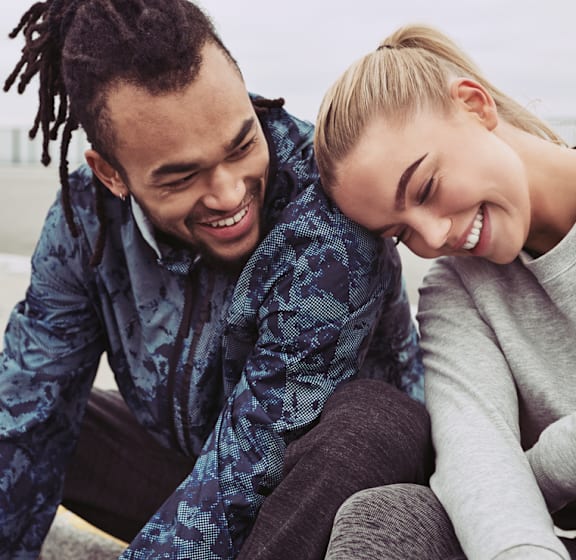 A man and a woman are sitting close together, both smiling and looking down at something out of frame.