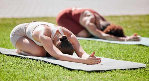 Two people doing yoga on mats in the grass.