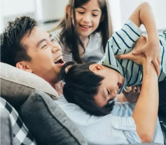 a father and two children laughing on a couch