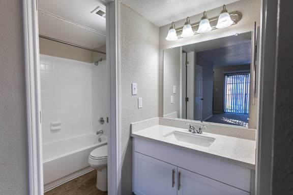 A white bathroom with a sink, mirror, and bathtub.