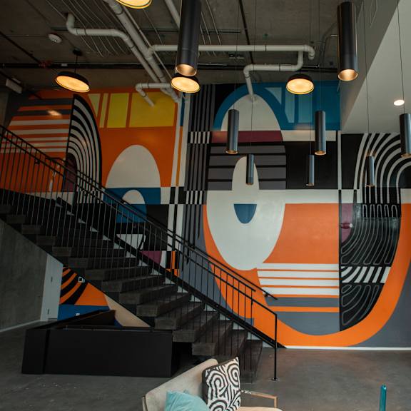 A staircase with a black railing and a wall with a large orange and white mural.