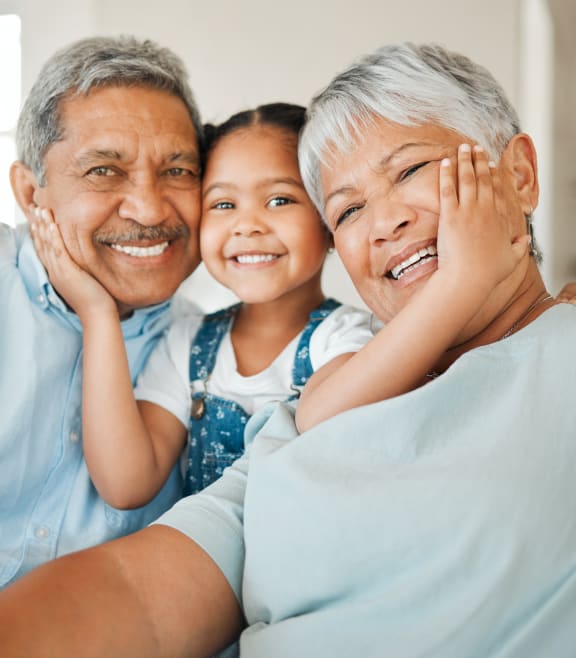 a young girl with her arms around her grandfather and grandmother as they sit on a couch at Emblem Alpharetta, Alpharetta, 30009