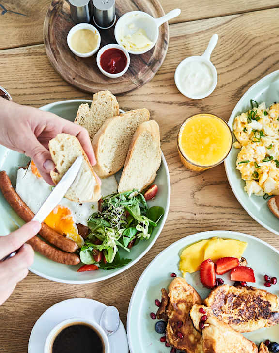 A group of people are having breakfast together with plates of eggs, toast and salad.