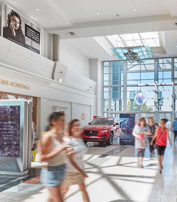 people walking through a shopping mall with a red car in the background