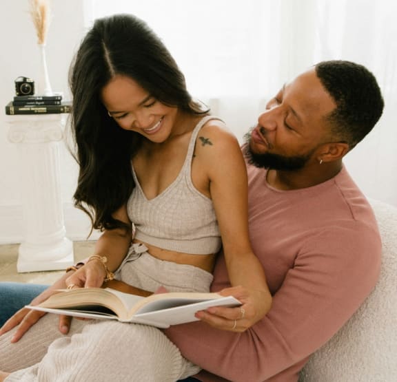 a man and woman sitting on a couch reading a book