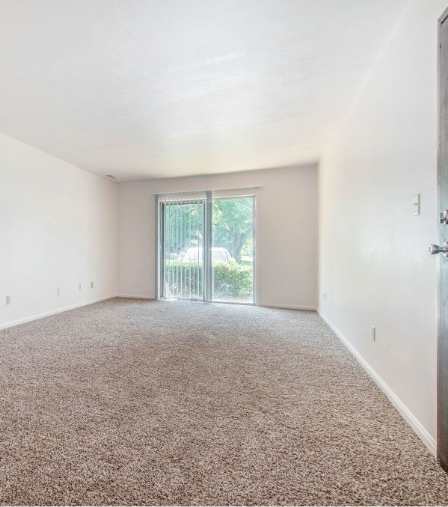 A spacious room with a carpeted floor and a sliding glass door leading to a balcony.