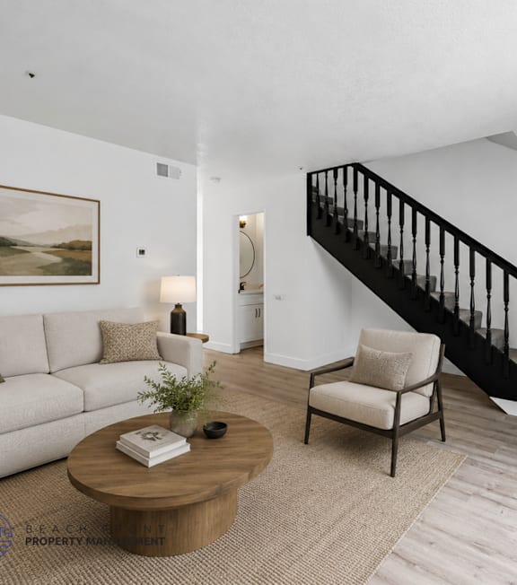 A living room with a white couch, a coffee table, a chair, a potted plant, and a painting on the wall.