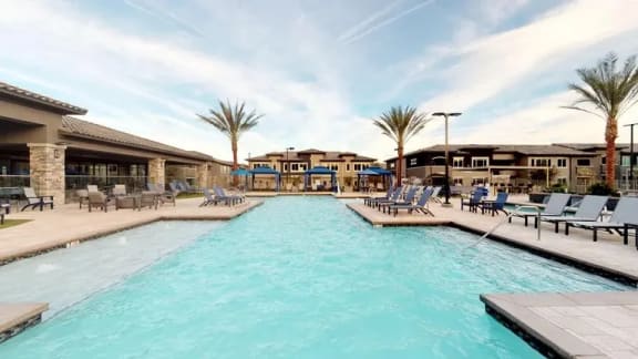 a large swimming pool with chairs and a building in the background