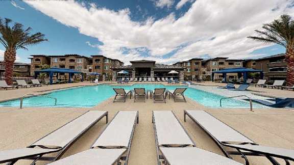 A large swimming pool surrounded by sun loungers and palm trees.