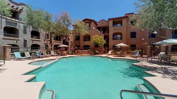 A swimming pool surrounded by lounge chairs and umbrellas in front of apartment buildings.