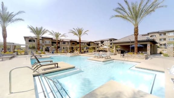 A swimming pool surrounded by lounge chairs and umbrellas in front of apartment buildings.